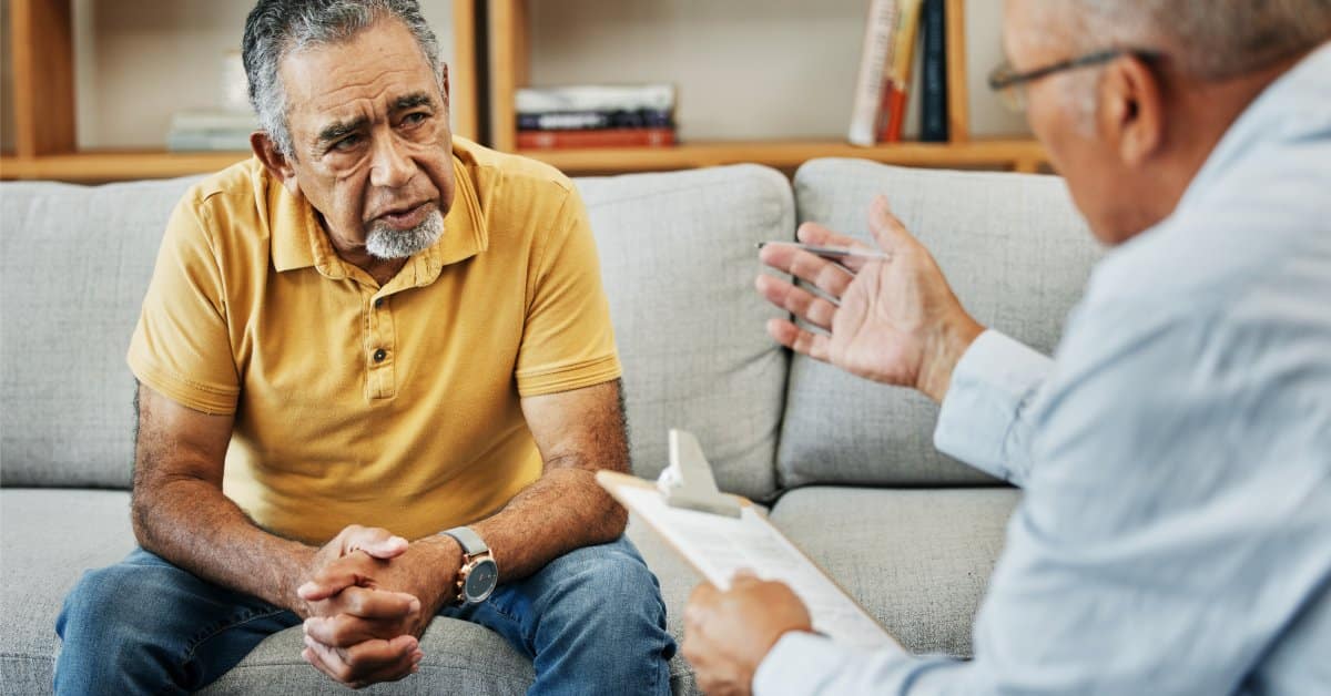 A man sits on a couch at a therapist's office and looks confused at the therapist talking and gesturing to them.