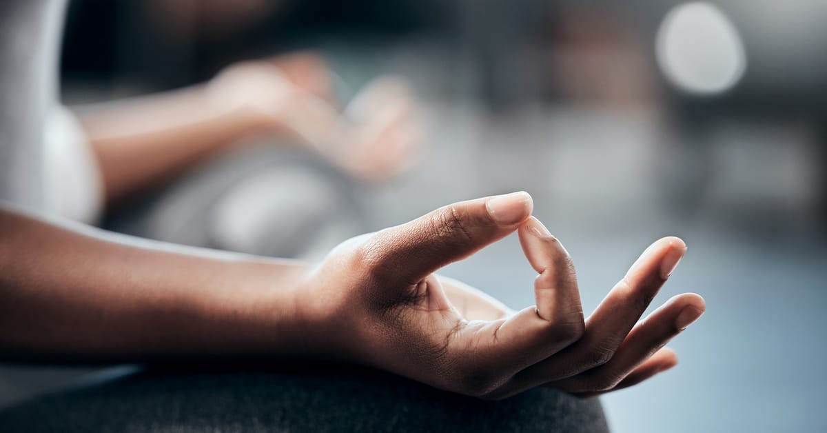 A close-up of a person's hand in the lotus pose while they practice meditation. They are wearing sweatpants.