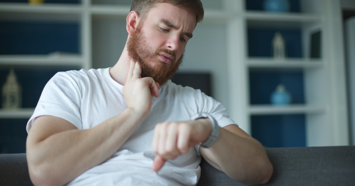 A man sits at home and checks his pulse. He has two fingers on his neck while he looks at the watch on his wrist.