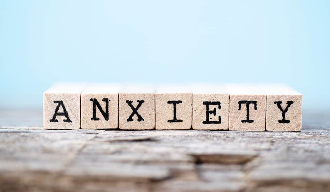 Several wooden blocks with letters spell out the word "anxiety" while they sit in front of a large blue background.