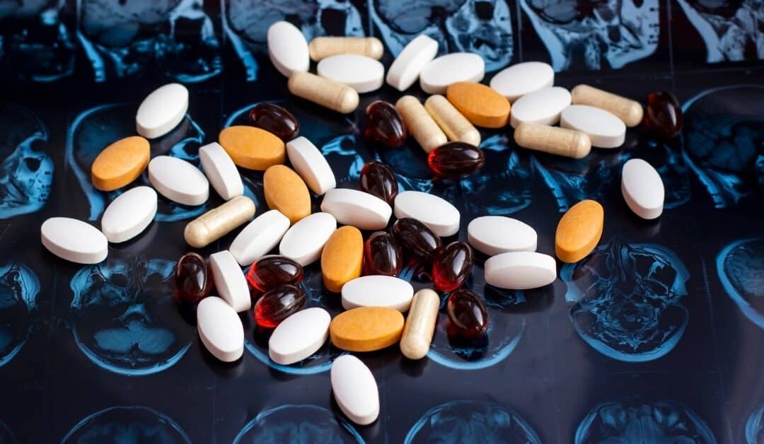 Several different pills lie on top of a background of MRI scans, featuring the human brain and the skull.